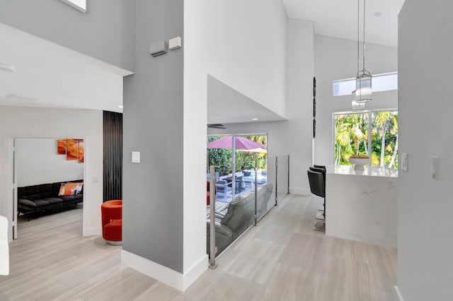 hallway with wood finished floors, baseboards, and a towering ceiling