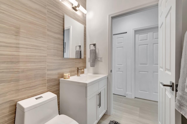 half bathroom featuring toilet, tile walls, and vanity