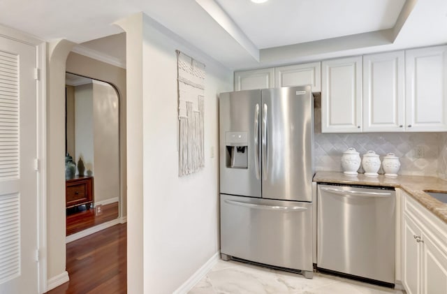 kitchen featuring light stone countertops, baseboards, arched walkways, decorative backsplash, and appliances with stainless steel finishes