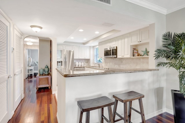 kitchen featuring dark wood finished floors, a peninsula, appliances with stainless steel finishes, a kitchen breakfast bar, and tasteful backsplash