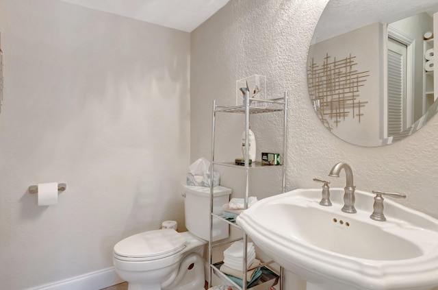 half bath featuring baseboards, toilet, a textured wall, and a sink