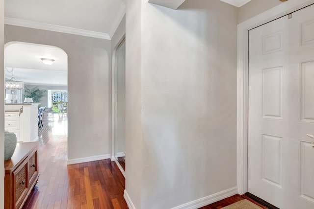 corridor with arched walkways, crown molding, dark wood-type flooring, and baseboards