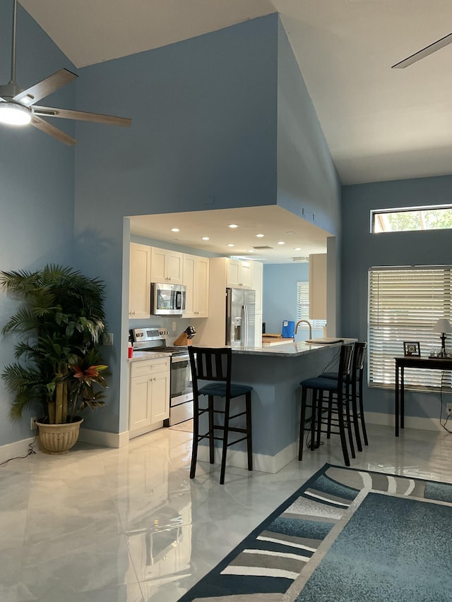 kitchen with stainless steel appliances, a kitchen breakfast bar, baseboards, and white cabinetry