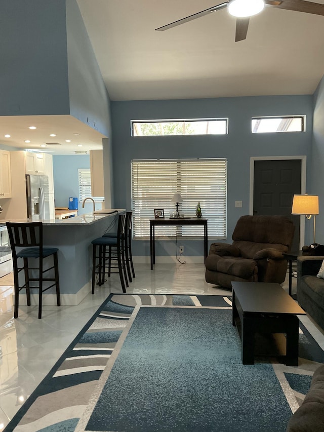 living area featuring a ceiling fan, a high ceiling, and baseboards