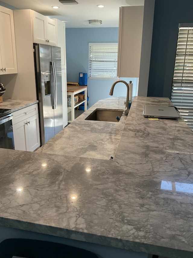 kitchen featuring visible vents, stone counters, white cabinets, stainless steel appliances, and a sink