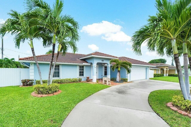 mediterranean / spanish house featuring an attached garage, driveway, a front lawn, and fence