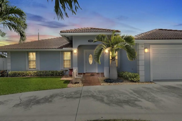 mediterranean / spanish-style home featuring an attached garage, stucco siding, concrete driveway, a tile roof, and a lawn