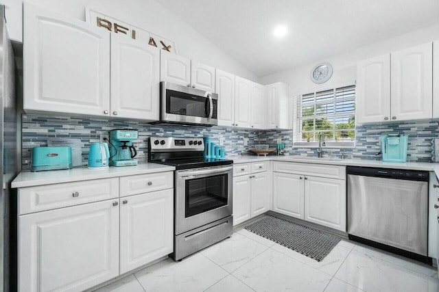 kitchen featuring lofted ceiling, a sink, white cabinets, appliances with stainless steel finishes, and marble finish floor