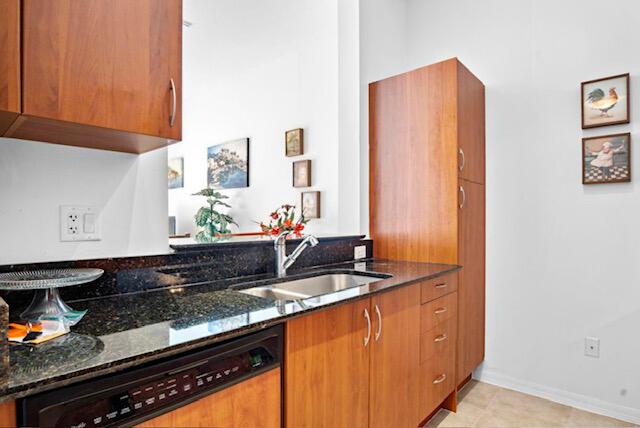 kitchen featuring a sink, dark stone countertops, paneled dishwasher, brown cabinetry, and baseboards