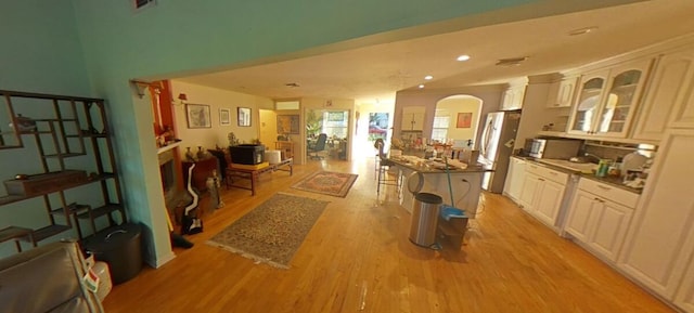 interior space featuring light wood-type flooring, tasteful backsplash, stainless steel appliances, arched walkways, and glass insert cabinets