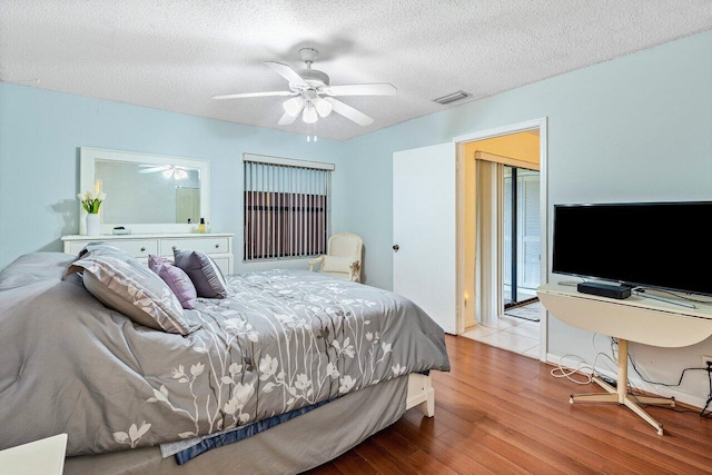 bedroom featuring visible vents, a textured ceiling, wood finished floors, and a ceiling fan