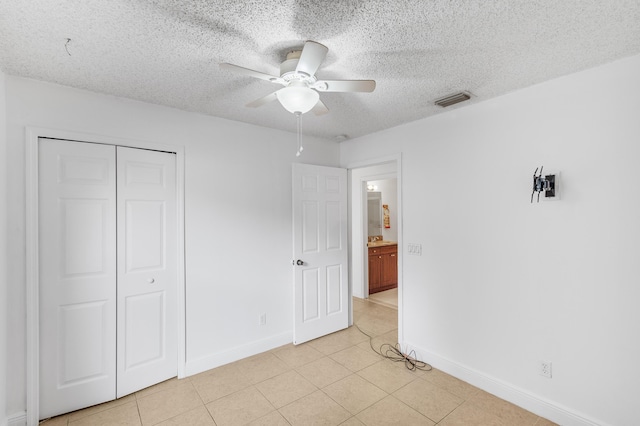 unfurnished bedroom with a closet, a textured ceiling, baseboards, and light tile patterned flooring