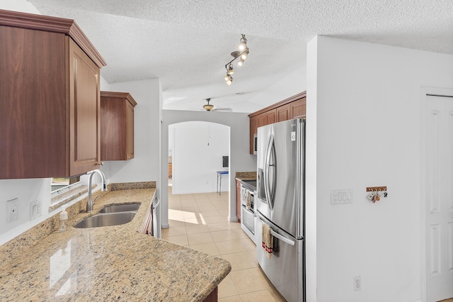 kitchen featuring light tile patterned floors, light stone countertops, a ceiling fan, a sink, and appliances with stainless steel finishes