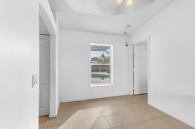 empty room featuring light tile patterned floors, baseboards, a textured ceiling, and a ceiling fan