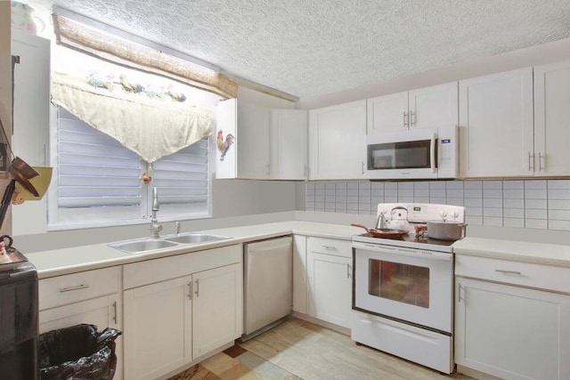 kitchen with light countertops, decorative backsplash, white appliances, a textured ceiling, and a sink