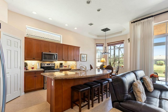 kitchen with a sink, backsplash, open floor plan, stainless steel appliances, and brown cabinetry