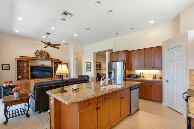 kitchen with a sink, light stone counters, an island with sink, and stainless steel appliances