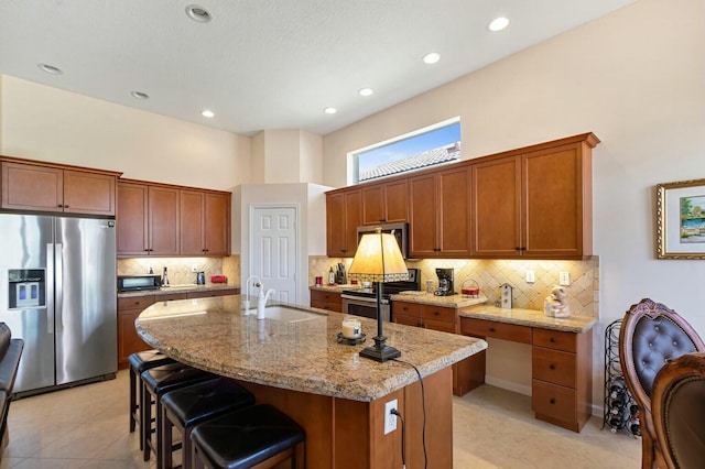 kitchen featuring light stone counters, a kitchen island with sink, a sink, appliances with stainless steel finishes, and a kitchen breakfast bar