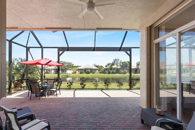 view of patio / terrace featuring a lanai, outdoor dining space, ceiling fan, and a water view