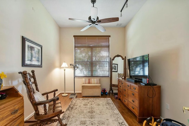 living area with dark wood finished floors, track lighting, a ceiling fan, and baseboards