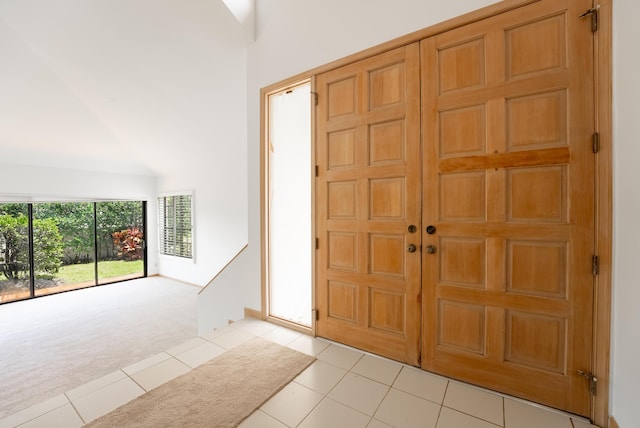 entryway featuring a high ceiling, light tile patterned floors, and light carpet