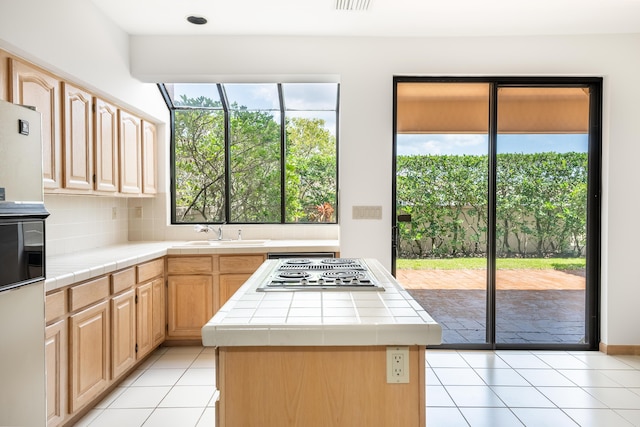 kitchen featuring light brown cabinetry, a sink, tile countertops, stovetop with downdraft, and light tile patterned floors