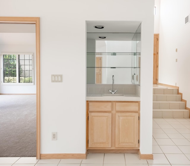 bar with visible vents, light carpet, a sink, light tile patterned flooring, and baseboards