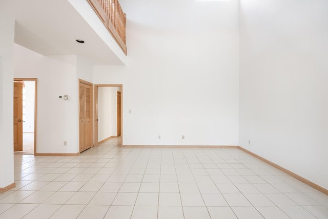 unfurnished room featuring light tile patterned flooring, baseboards, and a towering ceiling