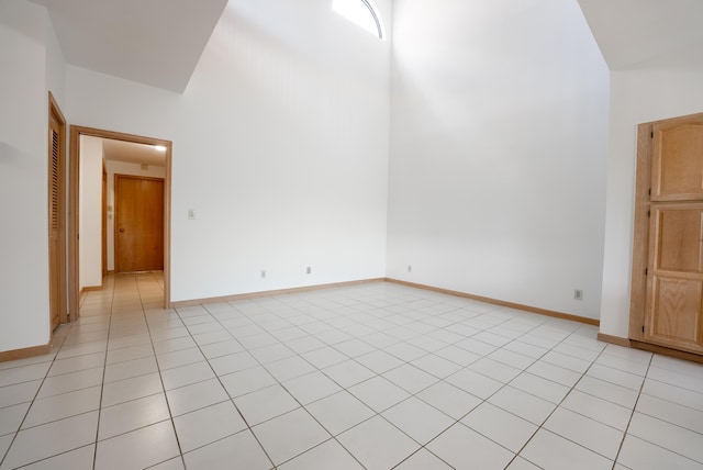 spare room featuring light tile patterned floors, baseboards, and a towering ceiling