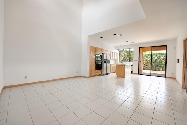 unfurnished living room with light tile patterned floors, visible vents, baseboards, and a towering ceiling