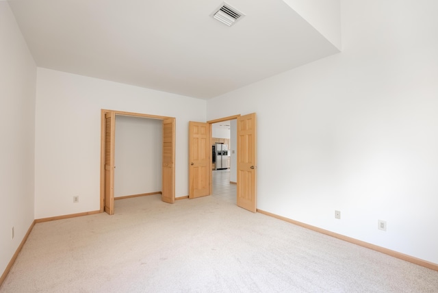 unfurnished bedroom with visible vents, light carpet, stainless steel refrigerator with ice dispenser, a closet, and baseboards