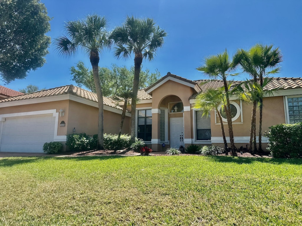 view of front of property with stucco siding, an attached garage, a front lawn, and a tiled roof