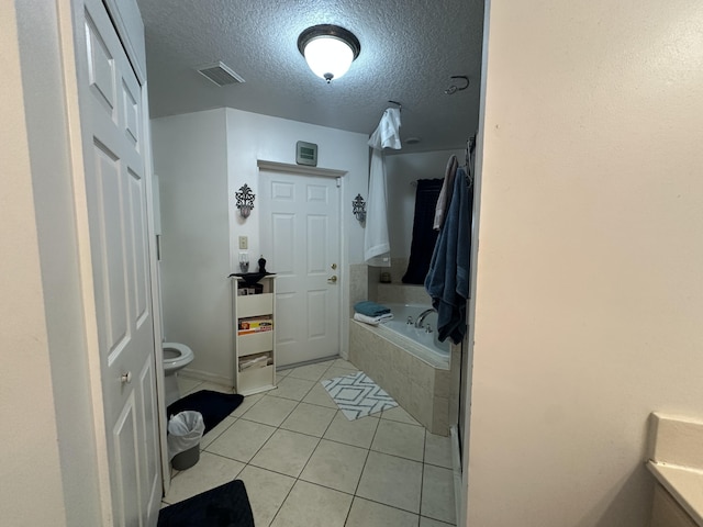 bathroom with visible vents, toilet, a textured ceiling, tile patterned flooring, and a relaxing tiled tub