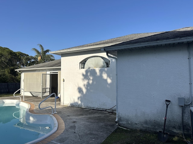 view of side of home with fence, a fenced in pool, roof with shingles, stucco siding, and a patio area