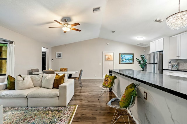 living room featuring vaulted ceiling, ceiling fan with notable chandelier, visible vents, and dark wood-type flooring