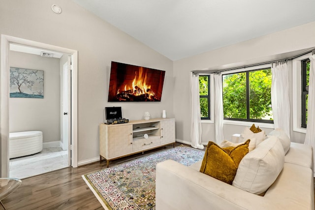 living room featuring visible vents, wood finished floors, baseboards, and vaulted ceiling