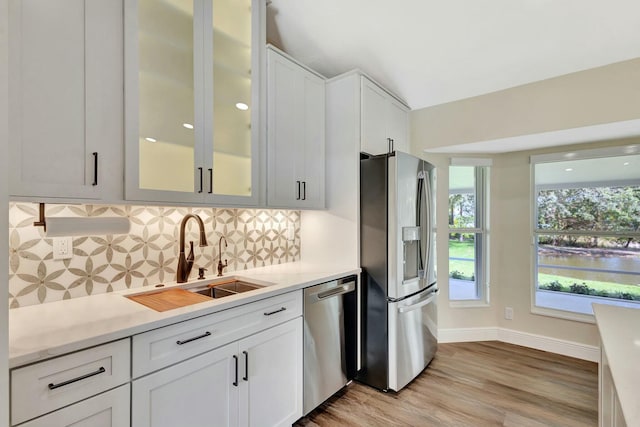 kitchen featuring a sink, decorative backsplash, light countertops, stainless steel appliances, and glass insert cabinets