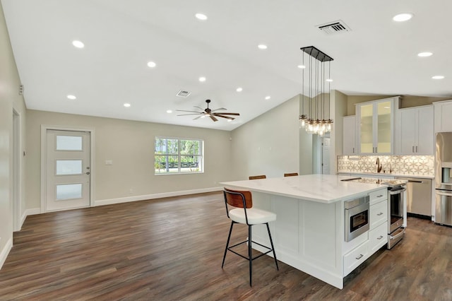 kitchen featuring visible vents, a kitchen island with sink, stainless steel appliances, vaulted ceiling, and white cabinets