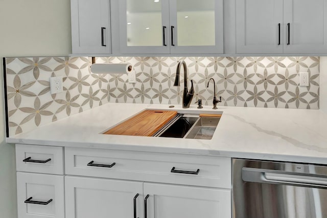 kitchen featuring decorative backsplash, a sink, stainless steel dishwasher, white cabinetry, and glass insert cabinets