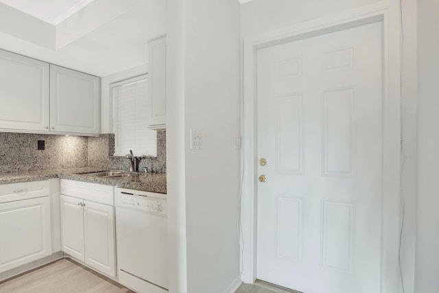 kitchen featuring light stone countertops, a sink, light wood-style floors, dishwasher, and tasteful backsplash