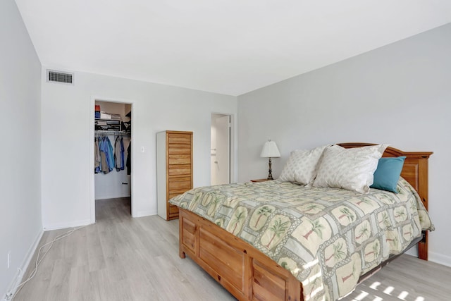 bedroom featuring baseboards, visible vents, light wood-style flooring, a closet, and a walk in closet