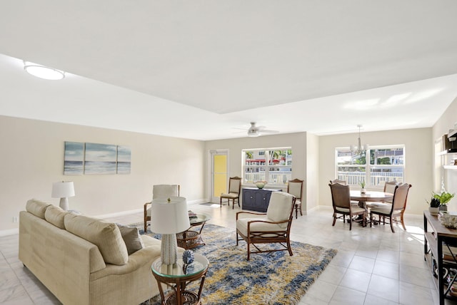 living area featuring light tile patterned floors, ceiling fan with notable chandelier, and baseboards