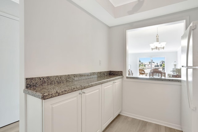 kitchen with a chandelier, pendant lighting, light wood-type flooring, freestanding refrigerator, and white cabinetry