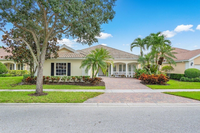 view of front of property with a front lawn, decorative driveway, a tile roof, and stucco siding