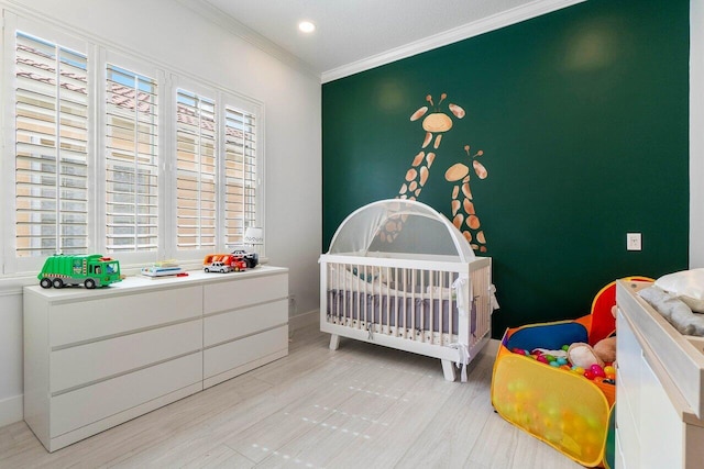 bedroom featuring a crib, light wood-style flooring, recessed lighting, crown molding, and an accent wall