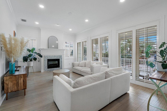 living area with a glass covered fireplace, visible vents, light wood-style floors, and ornamental molding