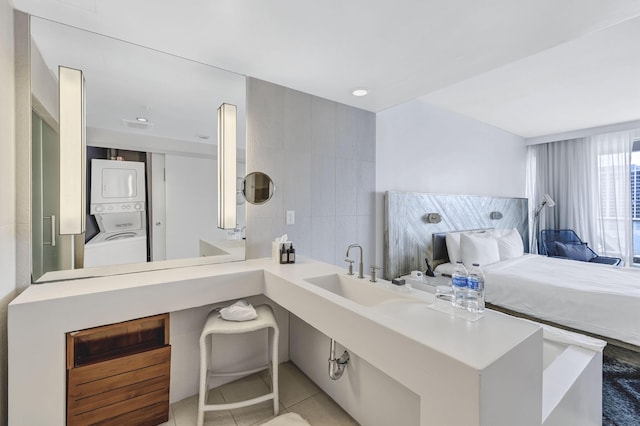 bathroom with tile walls, stacked washer / drying machine, a sink, and tile patterned flooring