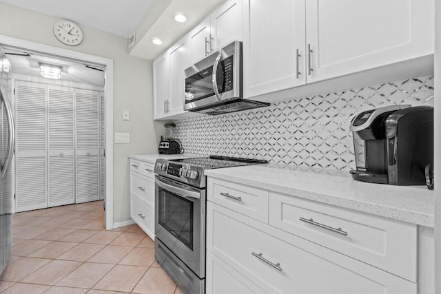 kitchen featuring light stone counters, light tile patterned floors, appliances with stainless steel finishes, white cabinetry, and backsplash