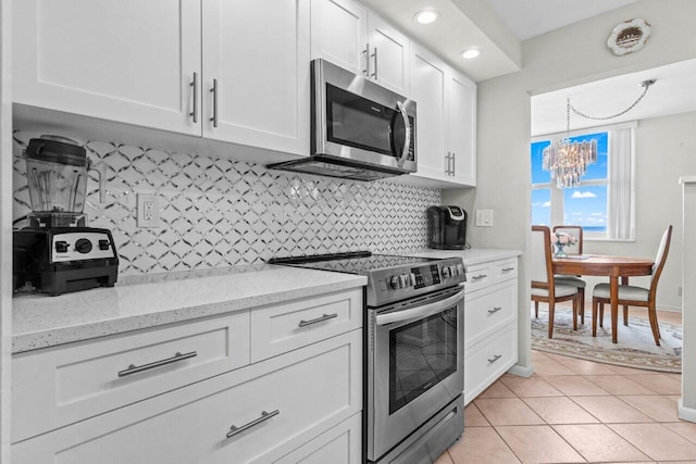 kitchen featuring backsplash, a chandelier, appliances with stainless steel finishes, light tile patterned flooring, and white cabinets