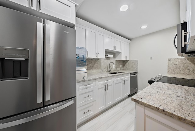 kitchen featuring light stone countertops, a sink, appliances with stainless steel finishes, white cabinetry, and backsplash